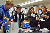 Photo of a teacher and three students standing around a block of desks.