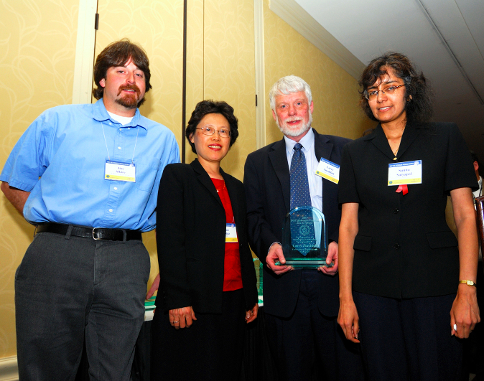 Photo of four U.S. Department of Energy employees, two men and two women, in business attire, standing in a hallway and facing the camera.