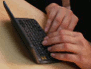Photo of a man's hands typing on a keyboard on a desk or table.