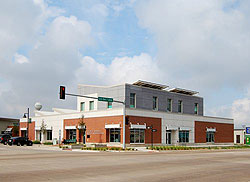 Photo of a brick and concrete building that has a second level constructed of concrete and a roof with solar panels on it. The building has windows along all sides on both levels. It is on a street corner with a street light labeled "US-54/400."