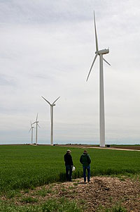 Photo of two men standing in a field in front of four large wind turbines.