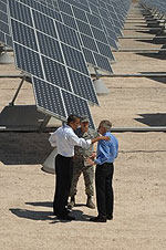 Photo of three males standing together in front of a row of ground-mounted solar photovoltaic trackers.