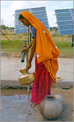 Photo of a woman in India using a water pump powered by photovoltaics to collect potable water.