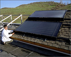 Photo of a researcher in a white lab coat crouched on a roof examining solar hot water heater panels.