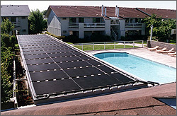 Photo of a large solar thermal collector on a roof and a pool with condominiums in the background.