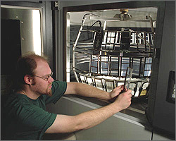 Photo of a researcher checking a sample from a testing chamber that subjects polymer glazing samples to UV light carefully matched to the natural light spectrum.