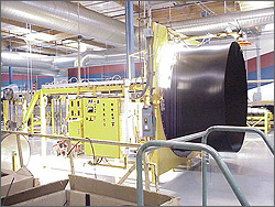 Photo of the inside of a warehouse with a large machine that produces solar pool-heating panels.