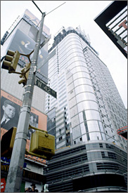 Photo of a skyscraper between two other skyscrapers, with visible advertising billboards and a utility pole and traffic light in the foreground.