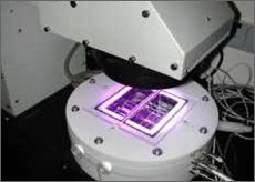 Photo of sample of reflective material on the stage of a characterization tool, with light illuminating the surface during a laboratory measurement.