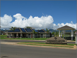 Photo of solar panels on roof of the Halsey Terrace Community Center, which is surrounded by green  grass and a kid's playground.  Clouds and trees can be seen in the background.