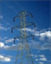 Photo of an electric tower, connected to transmission lines, with clouds and a blue sky in the background. 