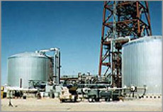 Photo of two large, gray storage system tanks at a power tower plant. The base of the tower can be seen in the background. Pipes leading into and out of the tanks carry heat-transfer fluid.