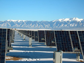 Photo of a field of one-axis tracking photovoltaic or solar electric panels at the SunEdison photovoltaic power plant near Alamosa, Colorado. Snowcapped mountains are visible in the background.