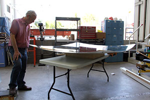 Photo of a man standing next to a table holding a large silver, square-shaped reflective material.