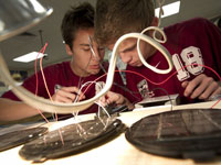 Photo of two young men working with wires coming from circular solar cells in a classroom laboratory.