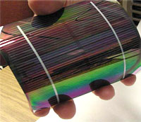 Photo of a hand bending a multi-colored, reflective solar cell.