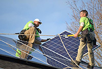Photo of two men in harnesses installing a solar panel on a rooftop.