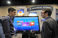 Photo of two men standing in front of a computer screen at an exhibit booth.