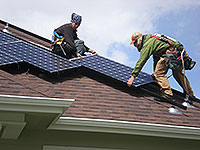 Photo of two workers installing solar photovoltaic panels on a residential roof.