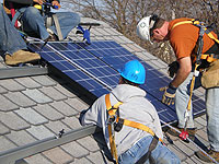 Photo of four workers installing solar panels on a sloped residential rooftop.