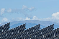 Photo of blue-gray photovoltaic panels with clouds in the blue sky overhead.