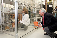 Photo of a male kneeling in a glass enclosure with wires and equipment.