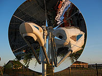 Photo of a circular mirrored dish-concentrator system that is reflecting a combined reactor-heat exchanger device.