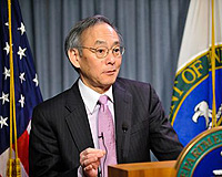 Photo of a man standing at a podium with flags in the background.