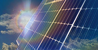 Image of an array of photovoltaic panels reflecting bright sunlight and clouds.