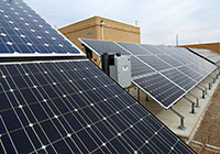 Photo of a row of solar photovoltaic panels outdoors; an inverter is positioned in between two of the panels.