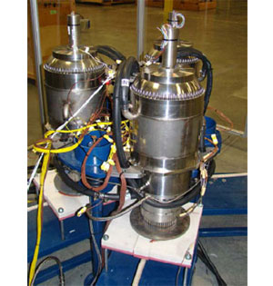 Photo of two silver, metallic cyclinders on a white platform.