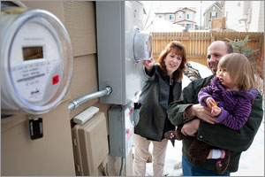 Photo of a woman, man, and child looking at a silver box on the outside of a home.
