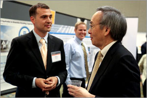 Photo of two men standing and speaking in front of a poster.