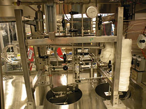 Photo of a lab with silver metal pipes, frames, and canisters connected together.