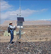 Image of a man in a hat adjusting controls on a ground antennae with solar panels on it.