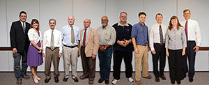Image of 11 adults, both male and female, standing in a low.