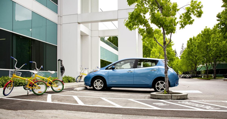 blue plug-in electric vehicle parked in front of charging station. Two bikes are in foreground.