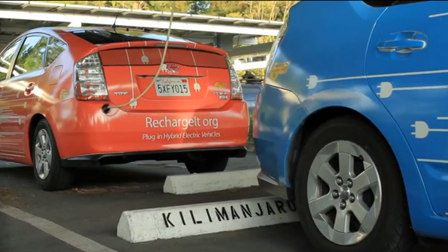 A red plug-in electric vehicle being charged. A blue PHEV is also in the picture.