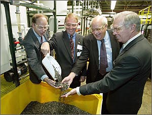 Photo of Ed Wall of the U.S. Department of Energy, Harvey Drucker of Argonne National Laboratory, and James Kolb of the American Plastics Council watching Richard T. Gutowski of DaimlerChrylser Co. pouring automotive plastics that have been cleaned and sorted for recycling.