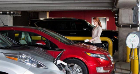 Woman charging red plug-in electric vehicle at a charging station.