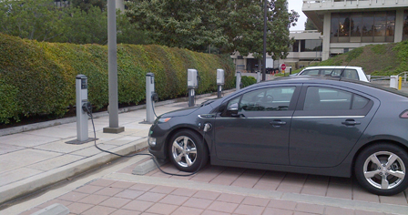 Grey plug-in electric vehicle at charging station. Additional chargers in the background.