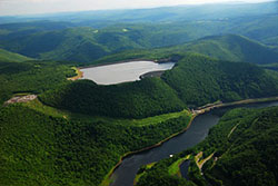 Photo of a reservoir next to a hydroelectric station, surrounded by wooded hills.