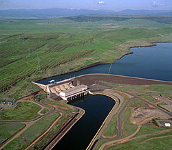 Photo of a hydropower plant located on a river with grassy hills around it.