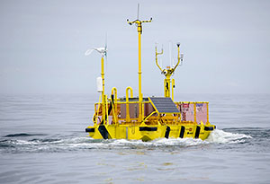 Photo of the NNMREC OceanSentinel, showing a the floating, metal test unit floating in the ocean.
