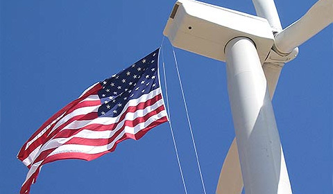 Photo of a wind turbine with an American flag hanging from it.