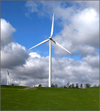 Photo of two multimegawatt wind turbines in a green field, blue sky with clouds in the background.