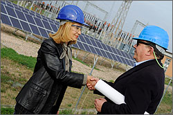 Photo of a man and a woman shaking hands in front of a photovoltaic (PV) array.