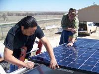 Photo of two men installing a photovoltaic panel on the roof of a trailer.