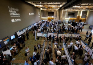 Photo taken from above showing event attendees interacting with eachother at poster stations in a large room.